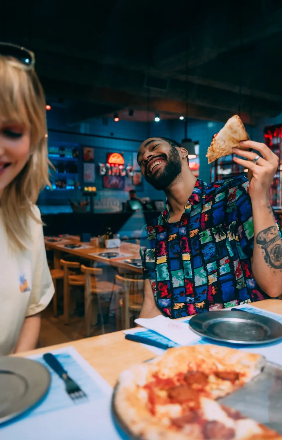Two friends laughing and having pizza at table