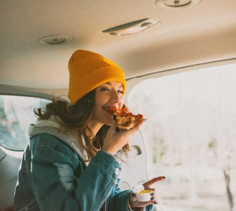 A young woman eating a piece of pizza in the car