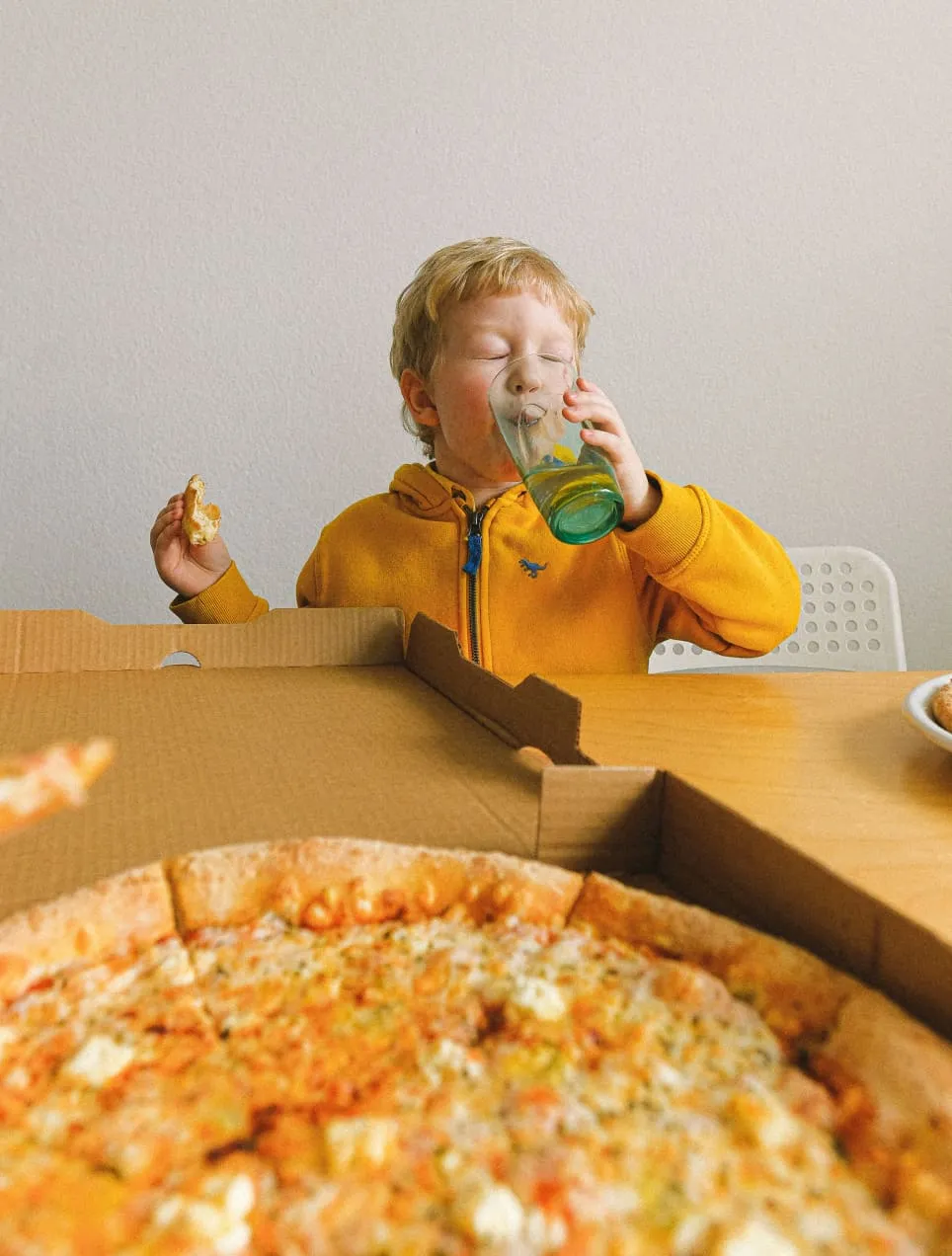 A little boy eating a big pizza and drinking water